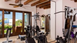 Une salle de sport équip ée de divers appareils d’exercice, dotée de grandes fenêtres et offrant une vue sur la verdure environnante.