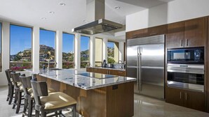 Une cuisine moderne dotée d’un grand îlot central, d’appareils électroménagers en acier inoxydable et offrant une vue sur une colline.