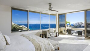 Une chambre moderne dotée d’un grand lit, d’un coin salon offrant une vue sur la mer et d’un balcon aménagé avec du mobilier d’extérieur.
