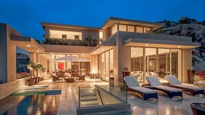 Une maison moderne à deux étages, dotée d’une piscine, d’un espace salon extérieur et de grandes fenêtres.