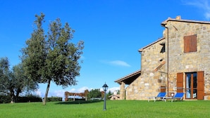 A stone building with a sloped roof, a wooden door, and a small balcony with a chair. - Agriturismo Le Sorgenti (Pitigliano)
