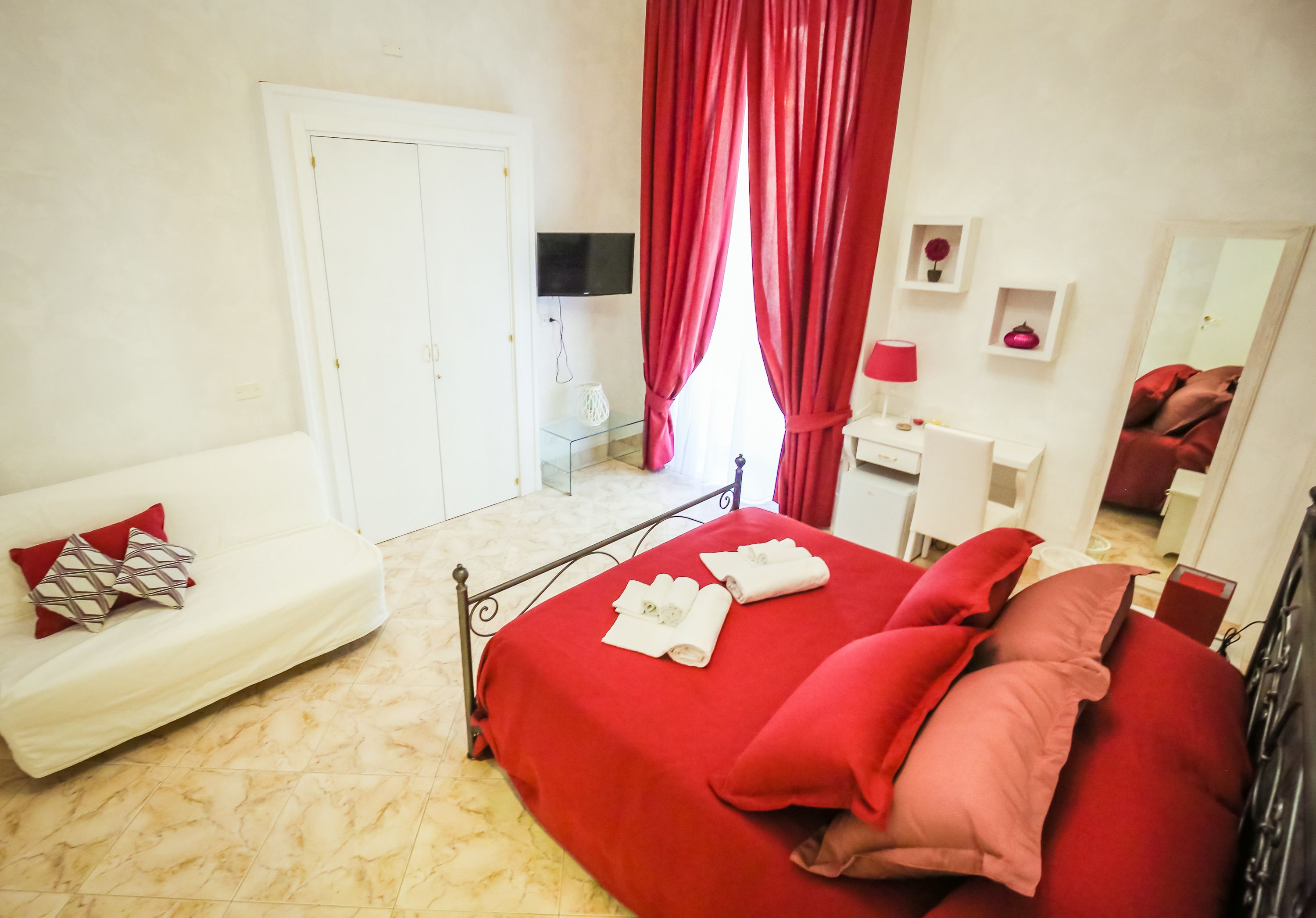 Un dormitorio con una cama, un sofá blanco, un escritorio, un televisor y un espejo.