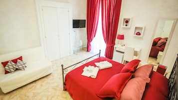 Un dormitorio con una cama, un sofá blanco, un escritorio, un televisor y un espejo.
