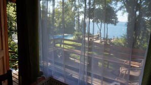 Vista desde una habitación con un ventanal grande que da a una piscina, una terraza y árboles.