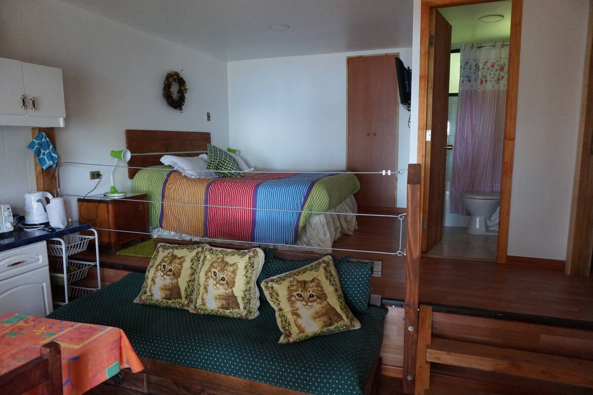 Ein kleines Schlafzimmer mit Etagenbett, einem Schreibtisch mit Wasserkocher, einem Kleiderschrank und einem durchgehenden Türspalt sichtbaren Badezimmer.