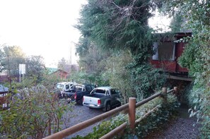 A parking area with several vehicles, including a white pickup truck and a black SUV, parked near a wooden fence and a stone wall. - Los Gualles de la Candelaria Apart Hotel (Pucón)