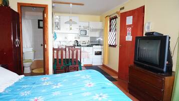 Una habitación pequeña con cama, televisión, kitchenette y baño.
