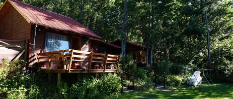 A cabin with a wooden deck and a swing chair in a forested area.