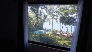 Vista a través de una ventana de un patio trasero con piscina, rodeado de árboles y una terraza de madera.