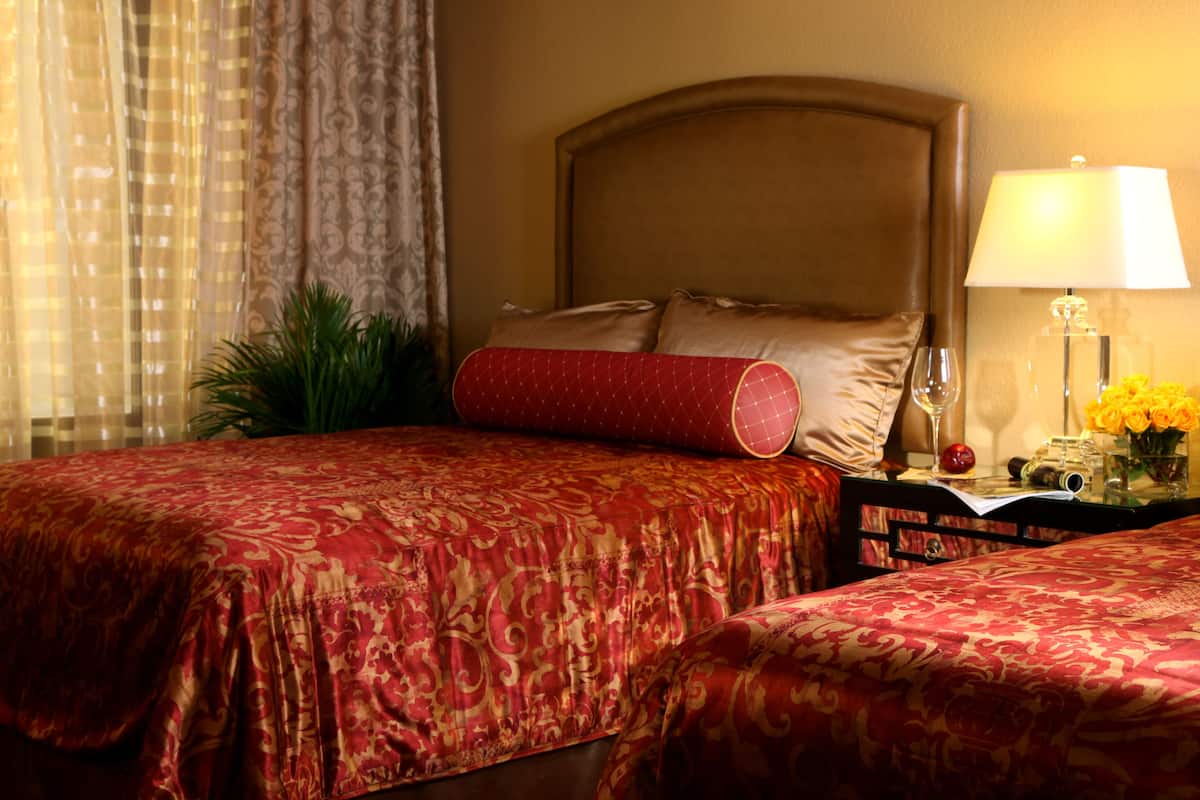 Een hotelkamer met twee bedden, een nachtkastje met een lamp en een raam met gordijnen.