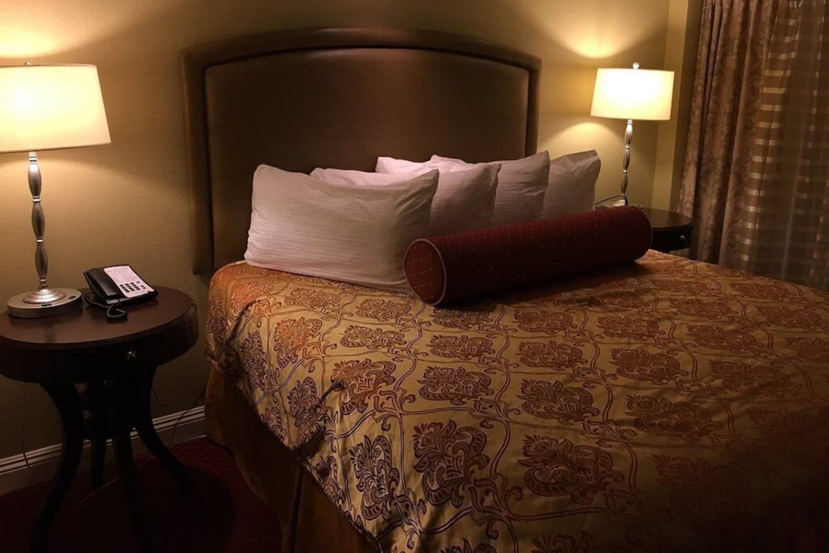 Een hotelkamer met een groot bed, twee bedlampen, een telefoon op een nachtkastje en een raam met gordijnen.