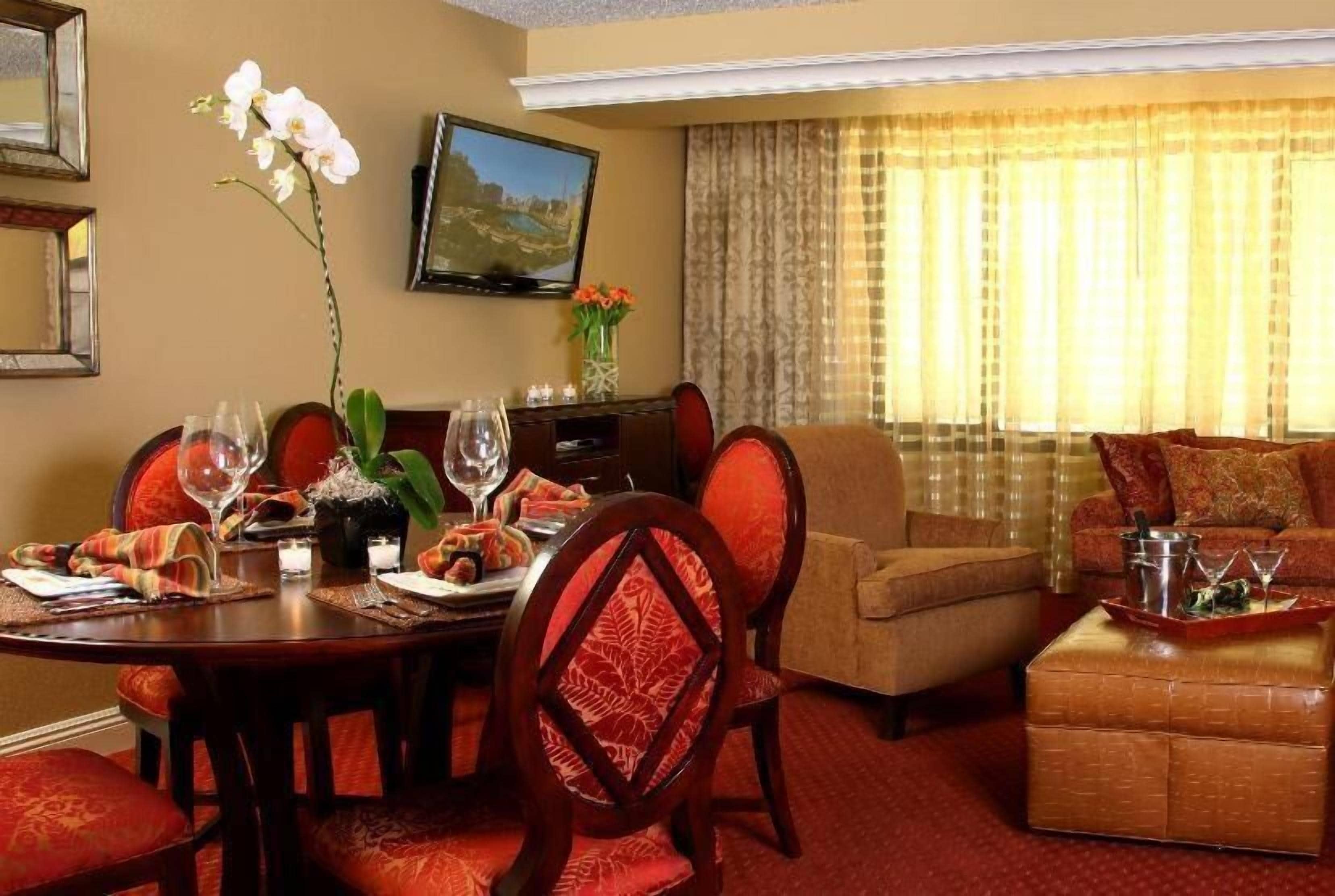 A hotel room with a dining table set for two, a sofa, and a television on the wall.