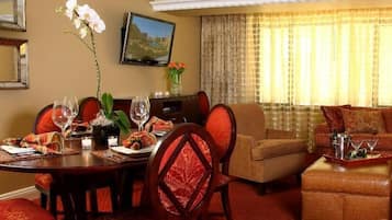 Une chambre d’hôtel avec une table à manger dressée pour deux personnes, un canapé et un téléviseur fixé au mur.