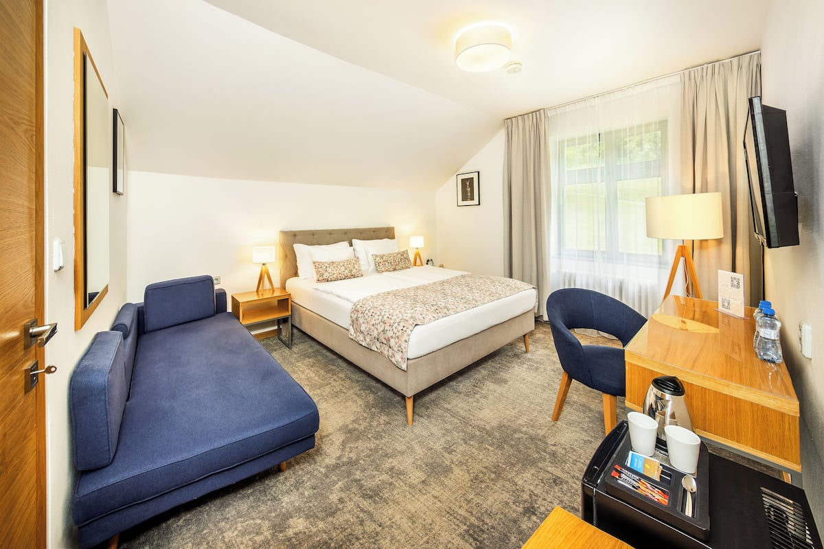 Een hotelkamer met een bed, een blauwe bank, een bureau met een lamp, een televisie en een koffiezetapparaat.