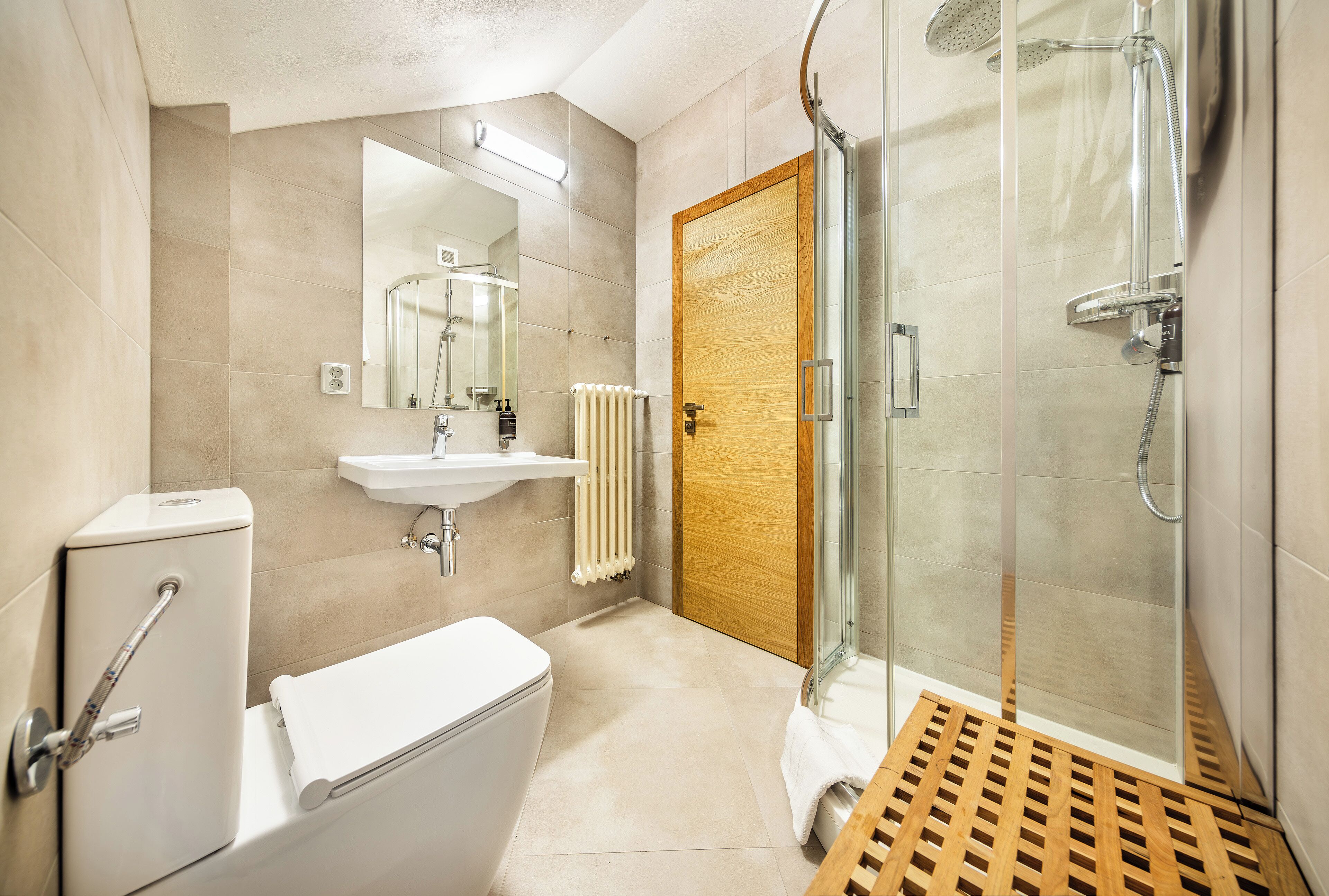 A modern bathroom with a toilet, sink, shower, and a wooden door.
