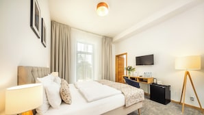 Une chambre d’hôtel équipée d’un lit, d’une table de chevet, d’une lampe, d’un bureau, d’une chaise et d’un téléviseur fixé au mur.
