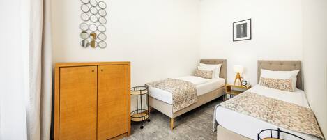 A hotel room with two beds, a wardrobe, a small round table, a lamp, and a wall-mounted mirror.