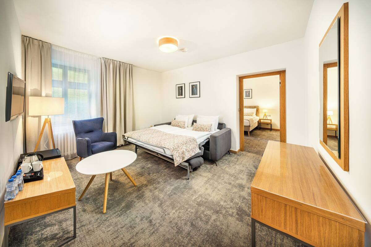 Een hotelkamer met een bed, een bureau, een stoel, een tafeltje en een grote spiegel.