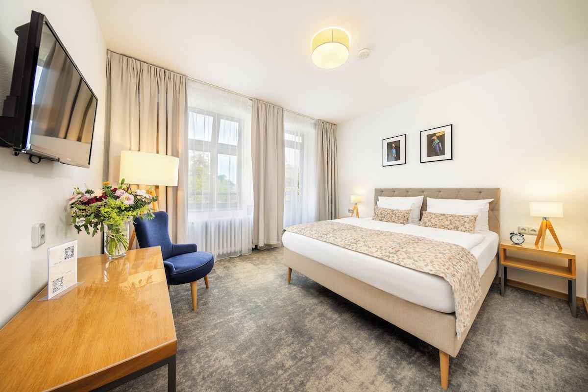 Een hotelkamer met een bed, bureau, stoel, televisie en een raam met gordijnen.