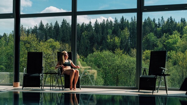 Un espace piscine avec vue sur une forêt, grâce à de grandes fenêtres.