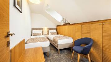 A compact room with two beds, a wooden wardrobe, a desk, and a blue chair.