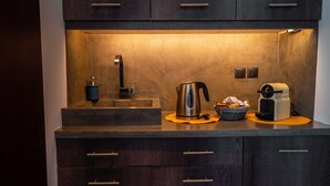 A modern kitchen with dark wood cabinets, a stainless steel sink, a kettle, a coffee maker, and a basket of bread. - The Athens Version Luxury Suites (Athens)