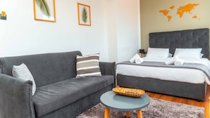 A modern hotel room with a grey sofa, a small round table, and a bed with white bedding. - The Athens Version Luxury Suites (Athens)