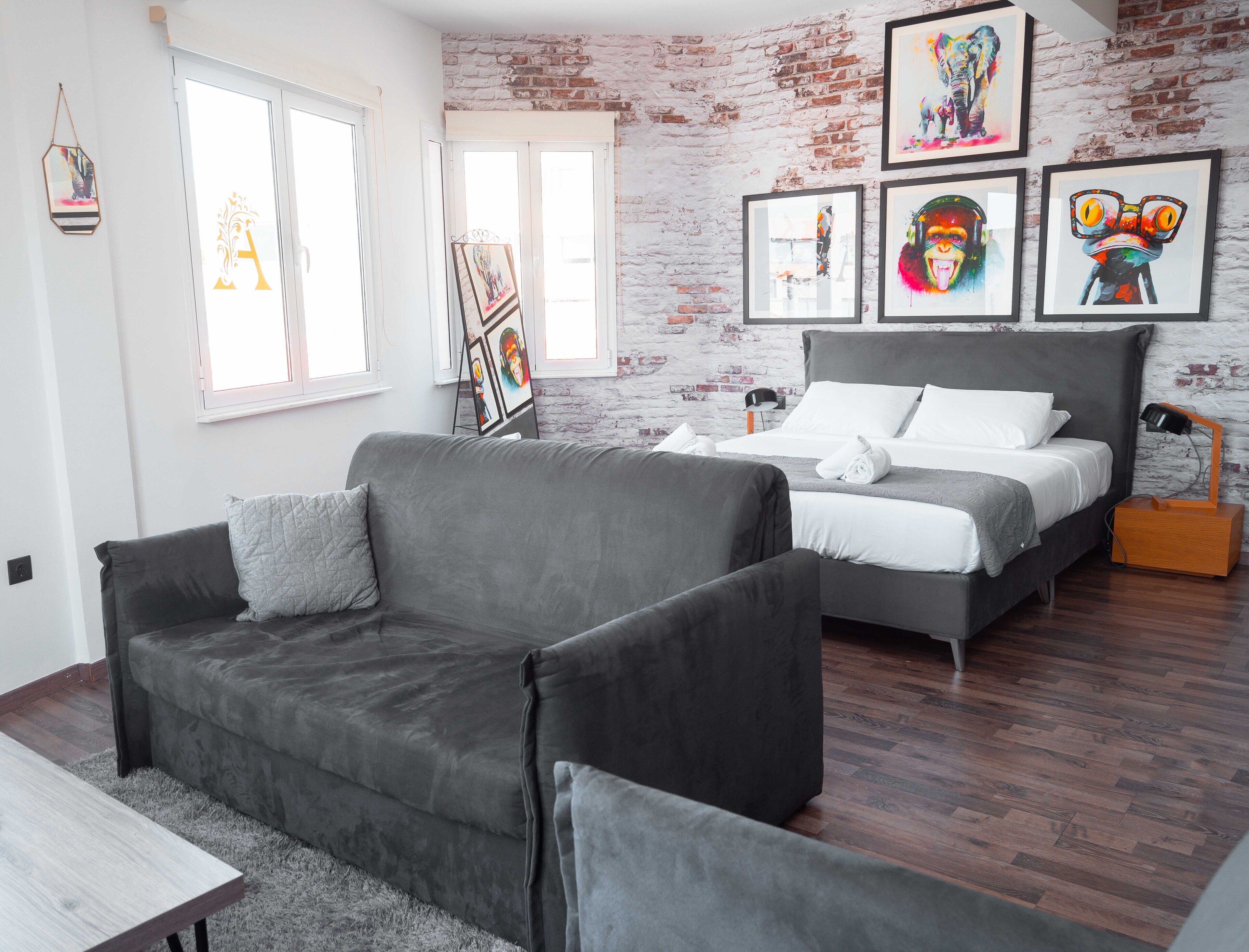 A modern bedroom with a gray sofa, a bed with white bedding, and a brick wall.