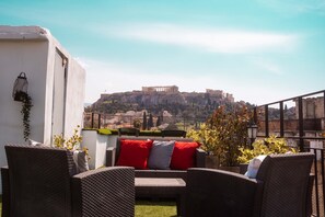 An outdoor seating area with wicker furniture and red cushions, overlooking a historic building on a hill. - The Athens Version Luxury Suites (Athens)