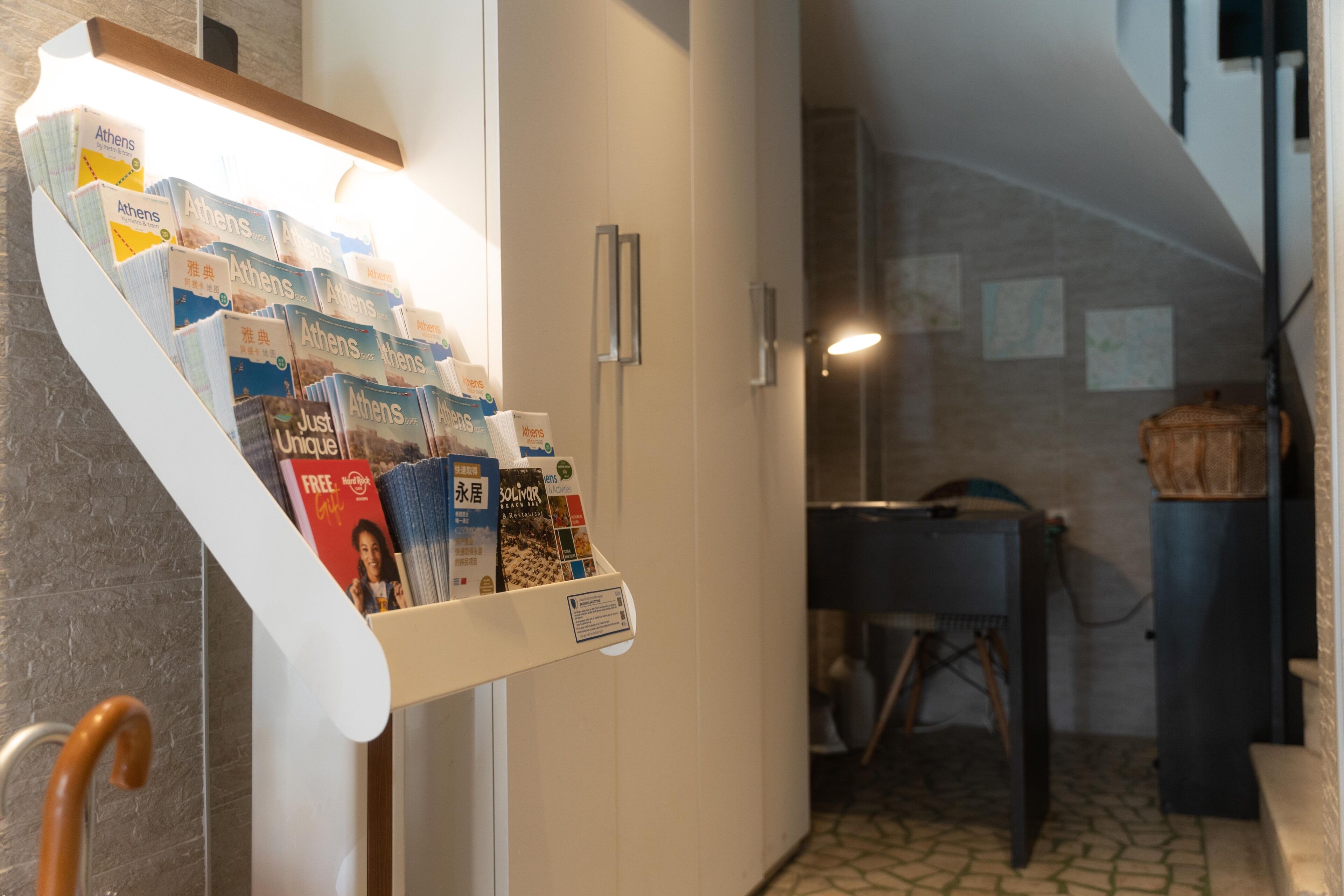 A hallway with a display of Athens travel brochures, a wooden cane, and a dining area with a table and chairs.