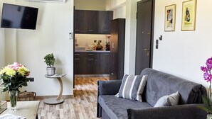 A modern living room with a grey sofa, a small round table, and a TV mounted on the wall. - The Athens Version Luxury Suites (Athens)