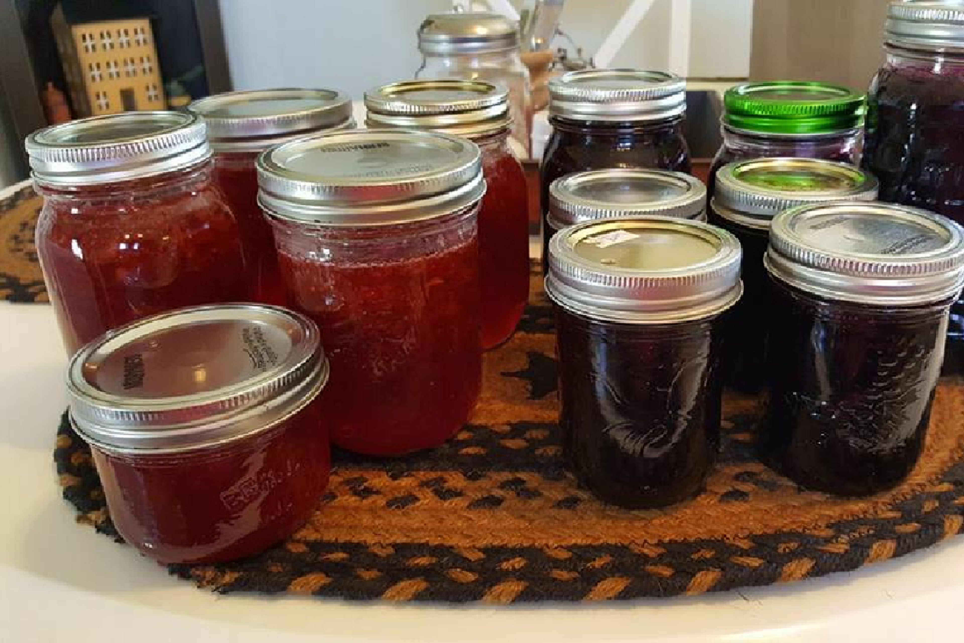 A collection of glass jars with metal lids, some with green lids, arranged on a woven mat.
