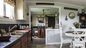 Una cocina con un lavamanos, una mesa de comedor con sillas y una puerta. Hay varios utensilios de cocina y adornos en las encimeras.
