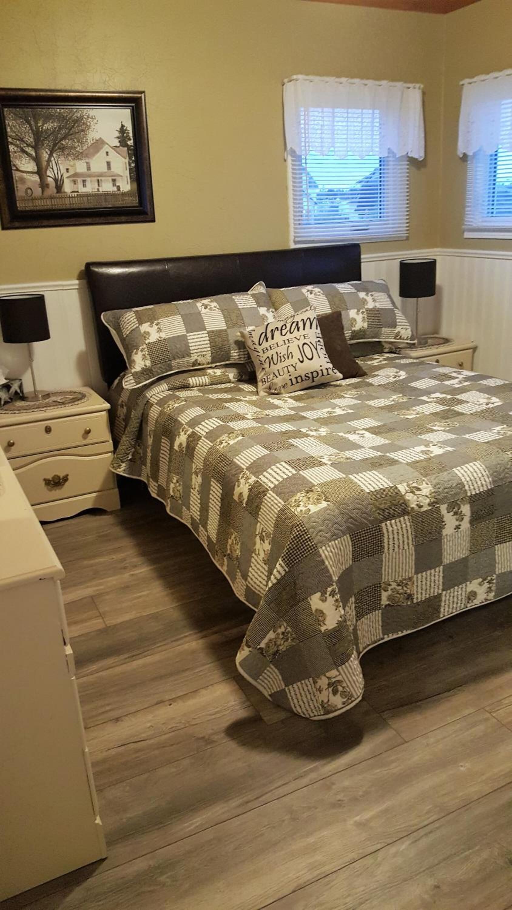 A bedroom with a bed, two bedside tables, a nightstand, a lamp, and a framed picture on the wall.