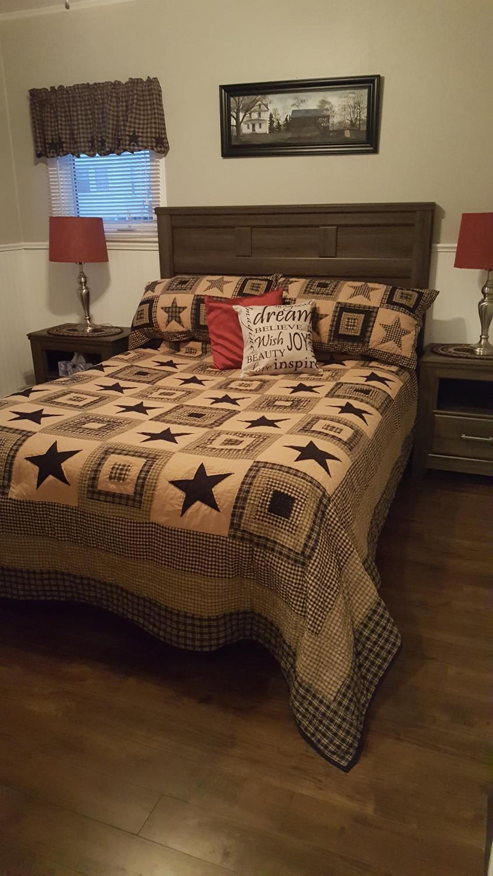 A bedroom with a large bed, a headboard, two bedside tables with lamps, a window with blinds, and a framed picture on the wall.