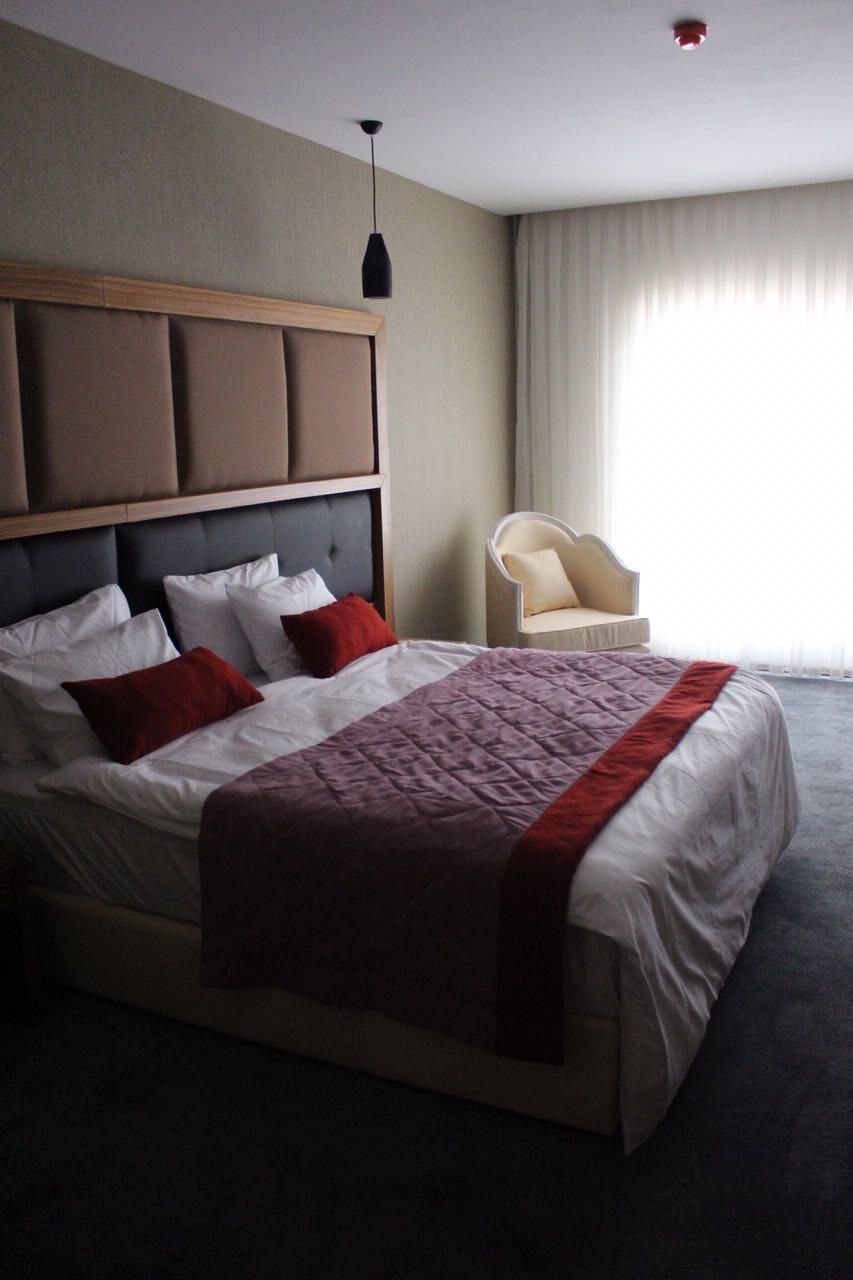 Et hotelværelse med en stor seng, en stol, et vindue med gardiner og en loftlampe.