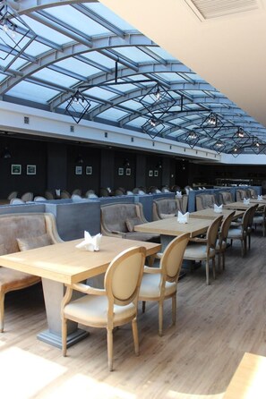 A restaurant with high ceilings, a glass ceiling, and wooden tables and chairs. - Sky Hotel (Baku)