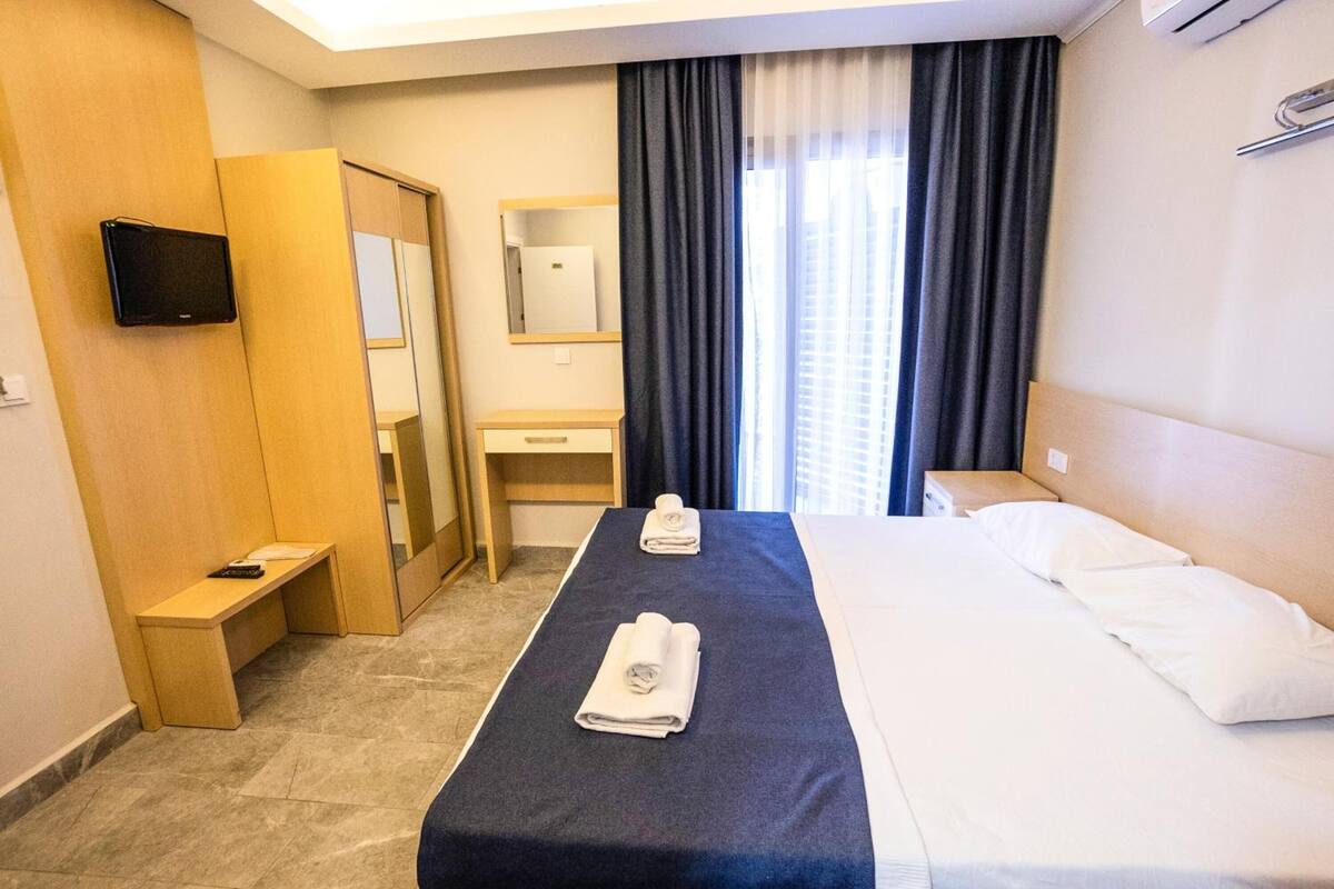 A hotel room with a bed, a bedside table, a TV, a mirror, a bathroom, and a window with curtains.