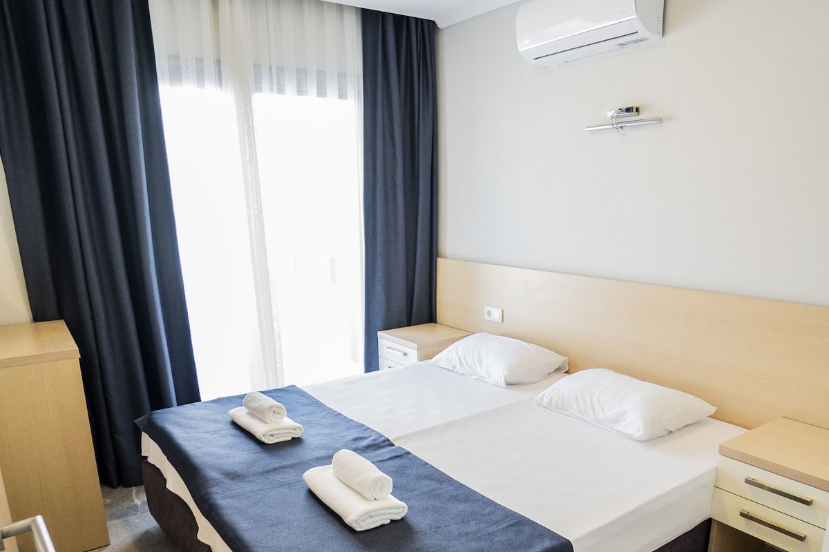 A hotel room with a large bed, a bedside table, a wardrobe, and a window with curtains.