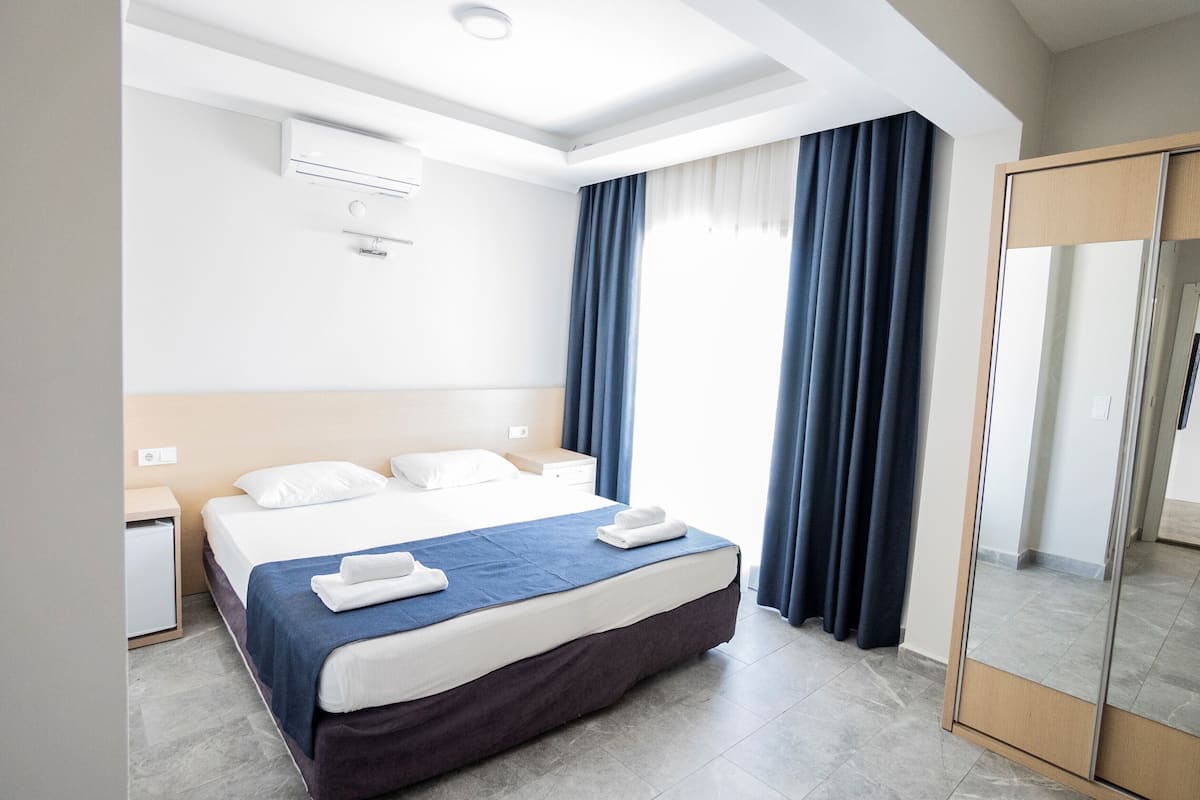 A hotel room with a large bed, a bedside table, an air conditioning unit, and a mirror.