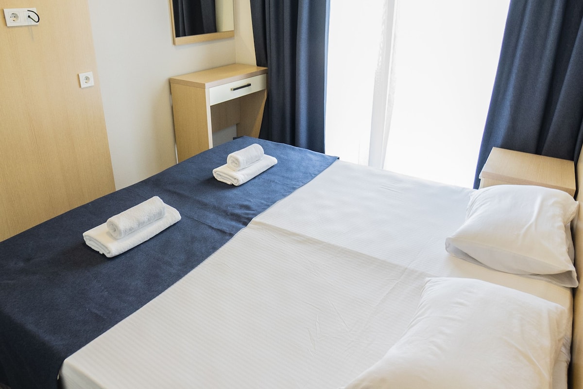 A hotel room with a bed, a desk, a mirror, and a window with curtains.