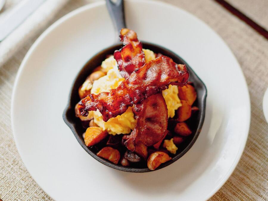 Un piatto da colazione con uova strapazzate, pancetta e patate.