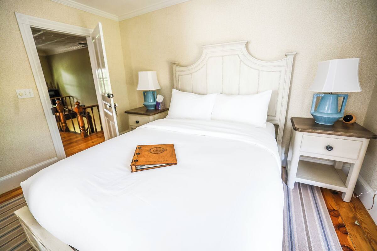 A neatly made bed with a book, a nightstand with a lamp, and a door leading to another room.