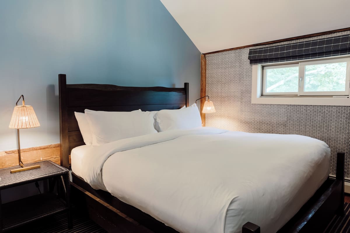 A neatly made bed with white linens, a dark wooden headboard, and a bedside lamp on a small table.