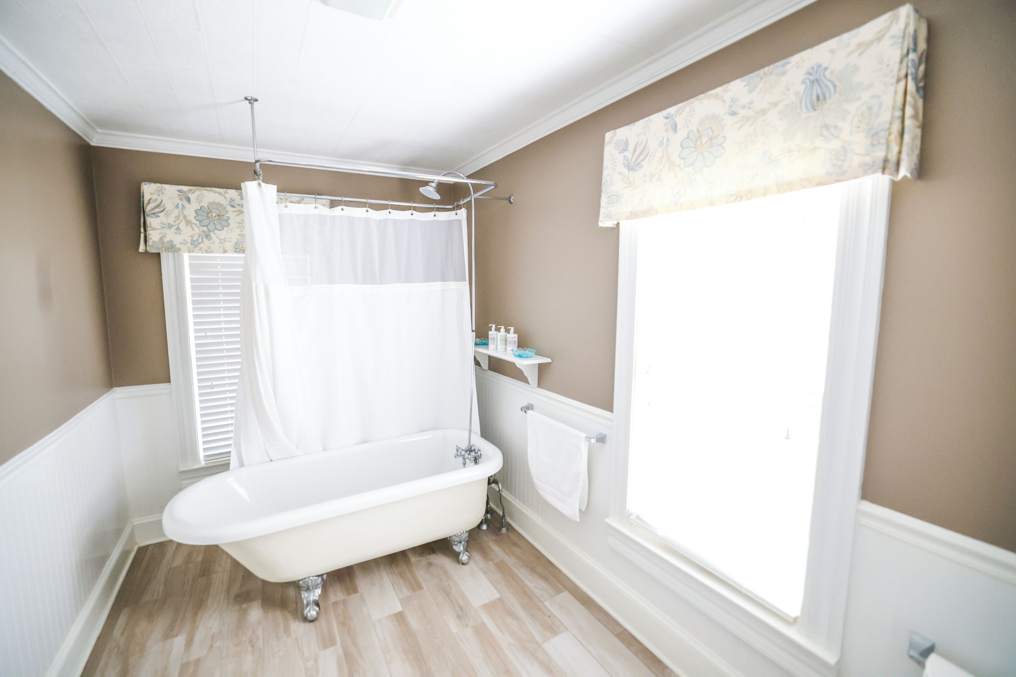 Une salle de bain avec une baignoire sur pieds, un rideau de douche, une fenêtre avec des stores et un radiateur.