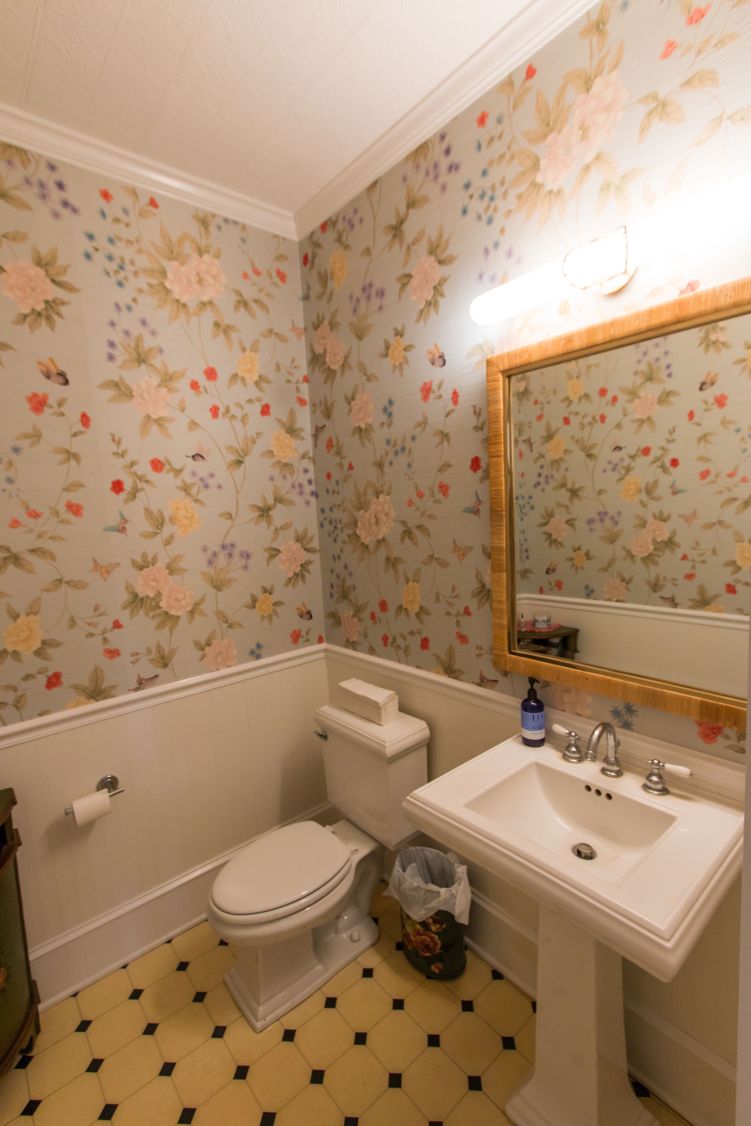 Un baño con papel tapiz floral, inodoro, lavabo y espejo.