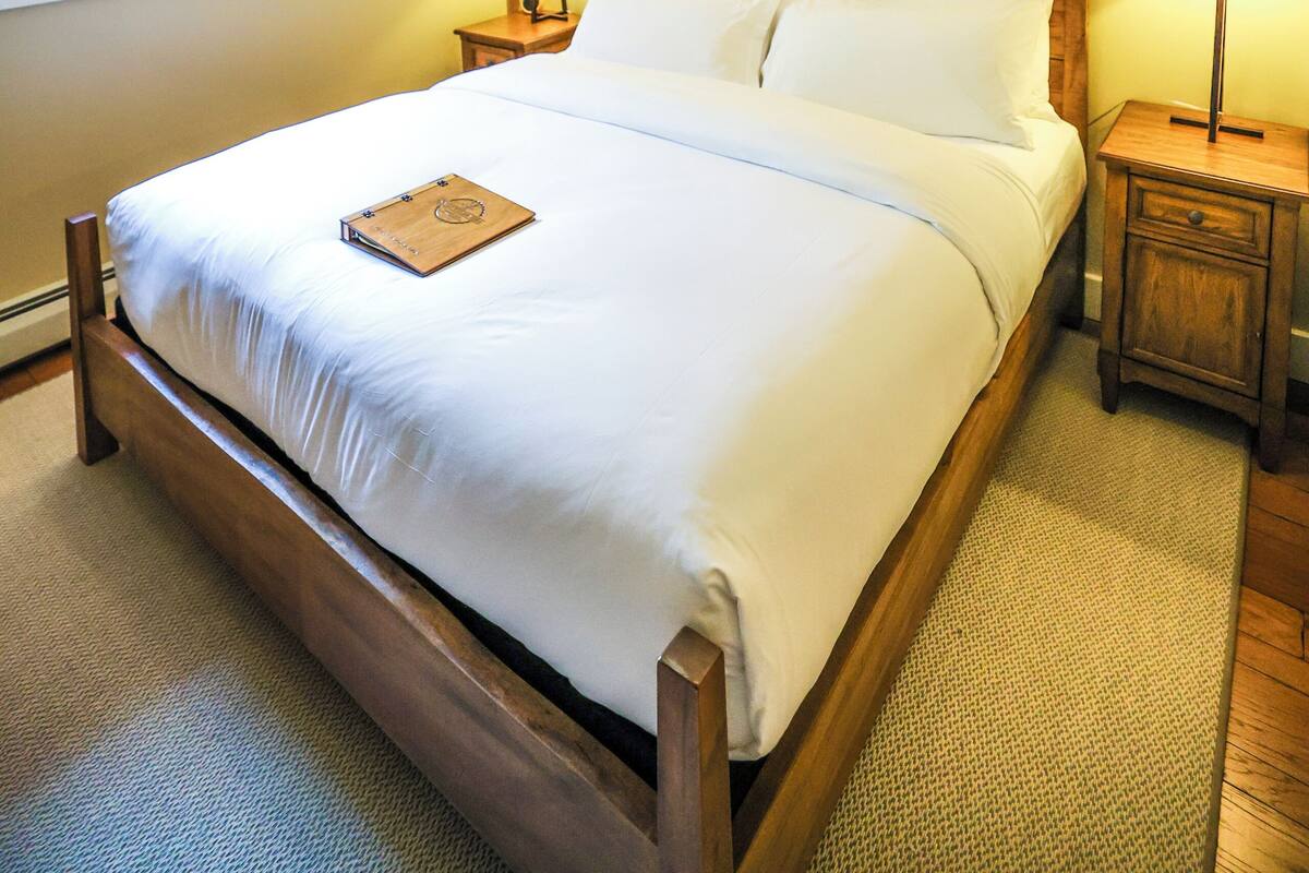 A bedroom with a wooden bed, a ceiling fan, two bedside lamps, and a window with a curtain.