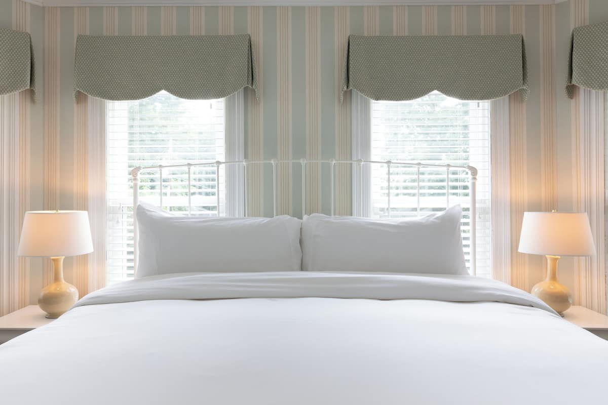 A hotel room with a large bed, two bedside lamps, and striped wallpaper.