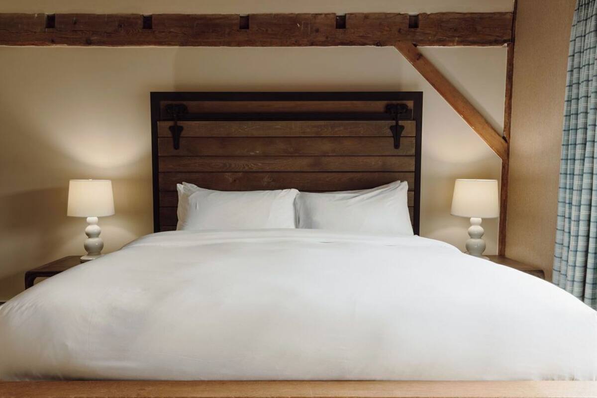A bed with a wooden headboard, two bedside lamps, and a plain wall.