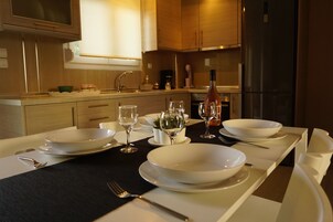 Una cocina moderna con armarios de madera, un refrigerador de acero inoxidable y una mesa de comedor con platos, tazones y copas de vino blancos.